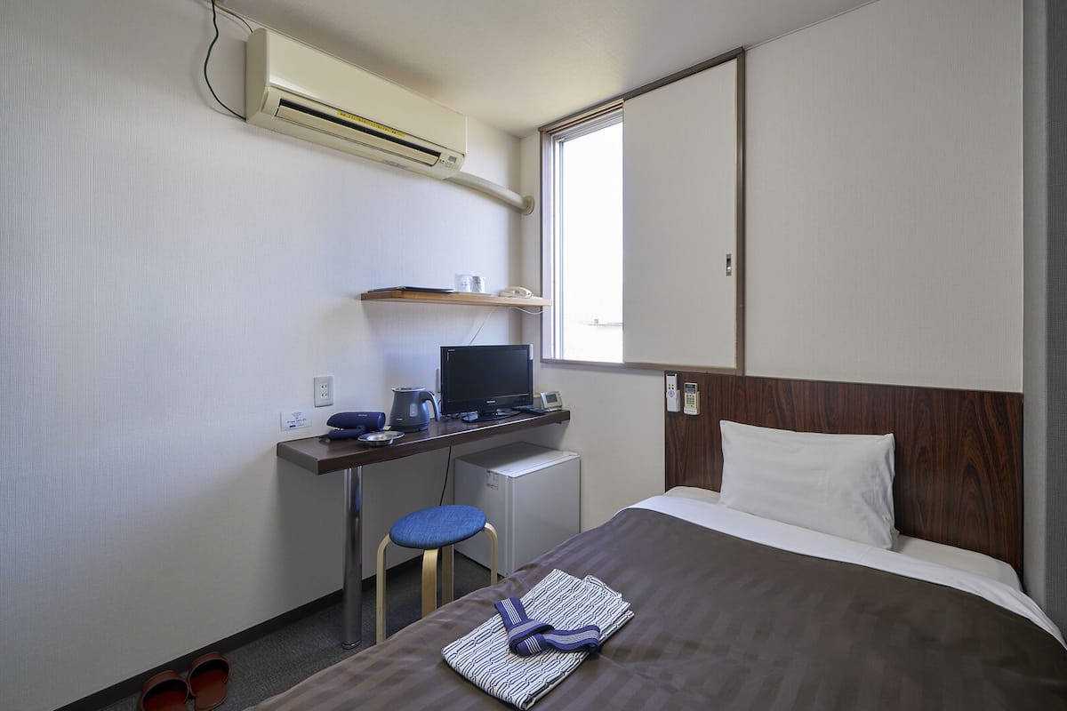 Ein Hotelzimmer mit Bett, Schreibtisch, Computer, Stuhl und Klimaanlage.