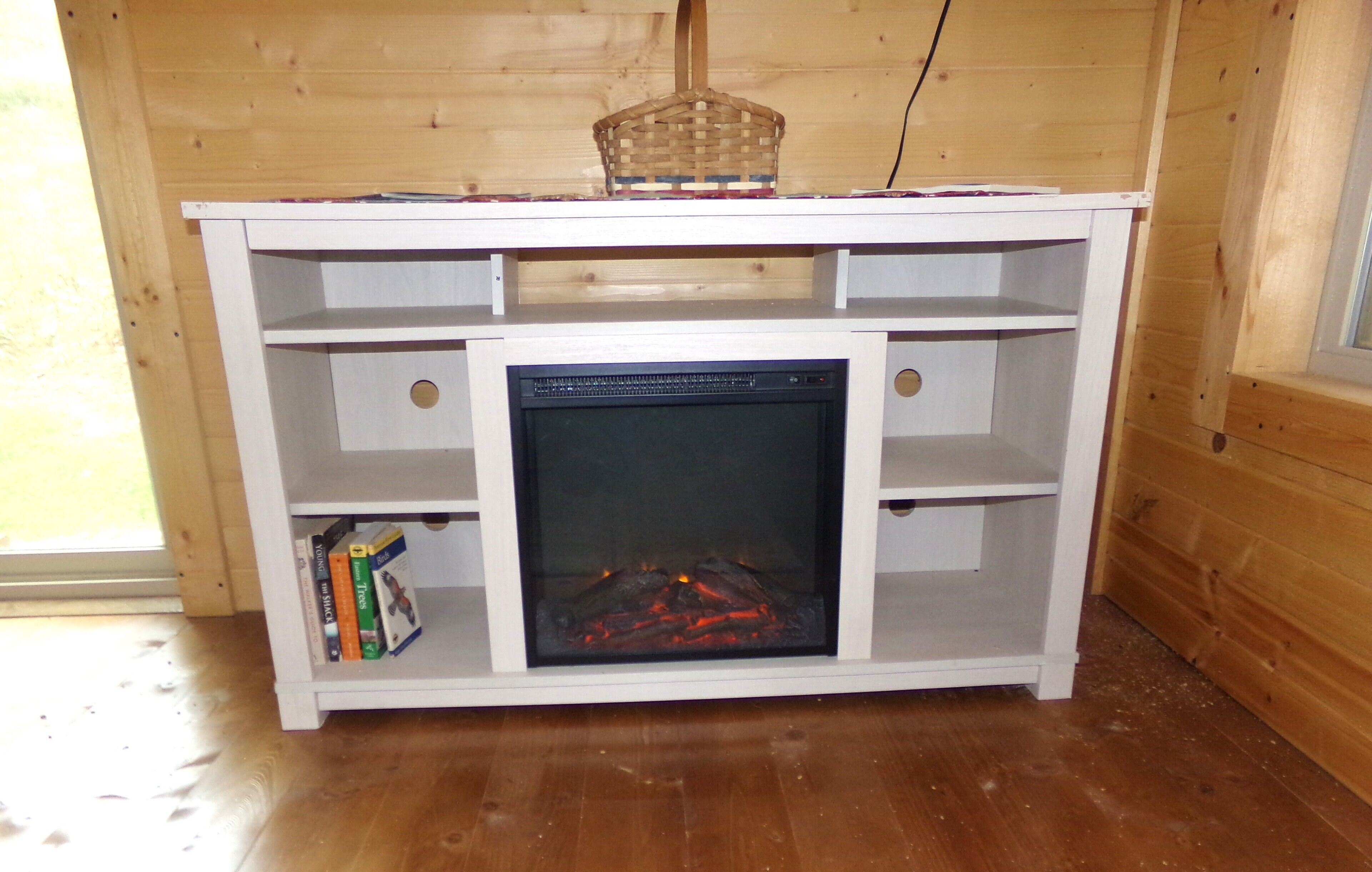A white entertainment unit with a fireplace, books, and a basket on top.