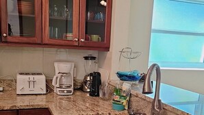 Une cuisine dotée de plans de travail en granit, d’un évier en acier inoxydable, d’un grille-pain, d’une machine à café et d’armoires en bois avec des portes en verre.
