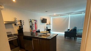 Uma cozinha moderna com uma ilha central, uma sala de jantar com mesa e cadeiras, e uma sala de estar com sofá e televisão.