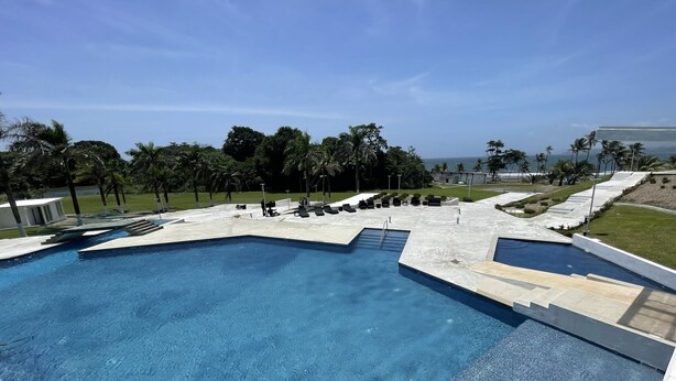 Uma grande piscina retangular com superfície de água azul e límpida, rodeada por um deck de concreto e espreguiçadeiras.