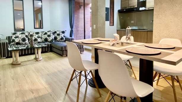 A modern dining area with a glass-top table, white chairs, and a black and white patterned sofa. - Apartamento,5 Parque de la 93 (Bogotá)