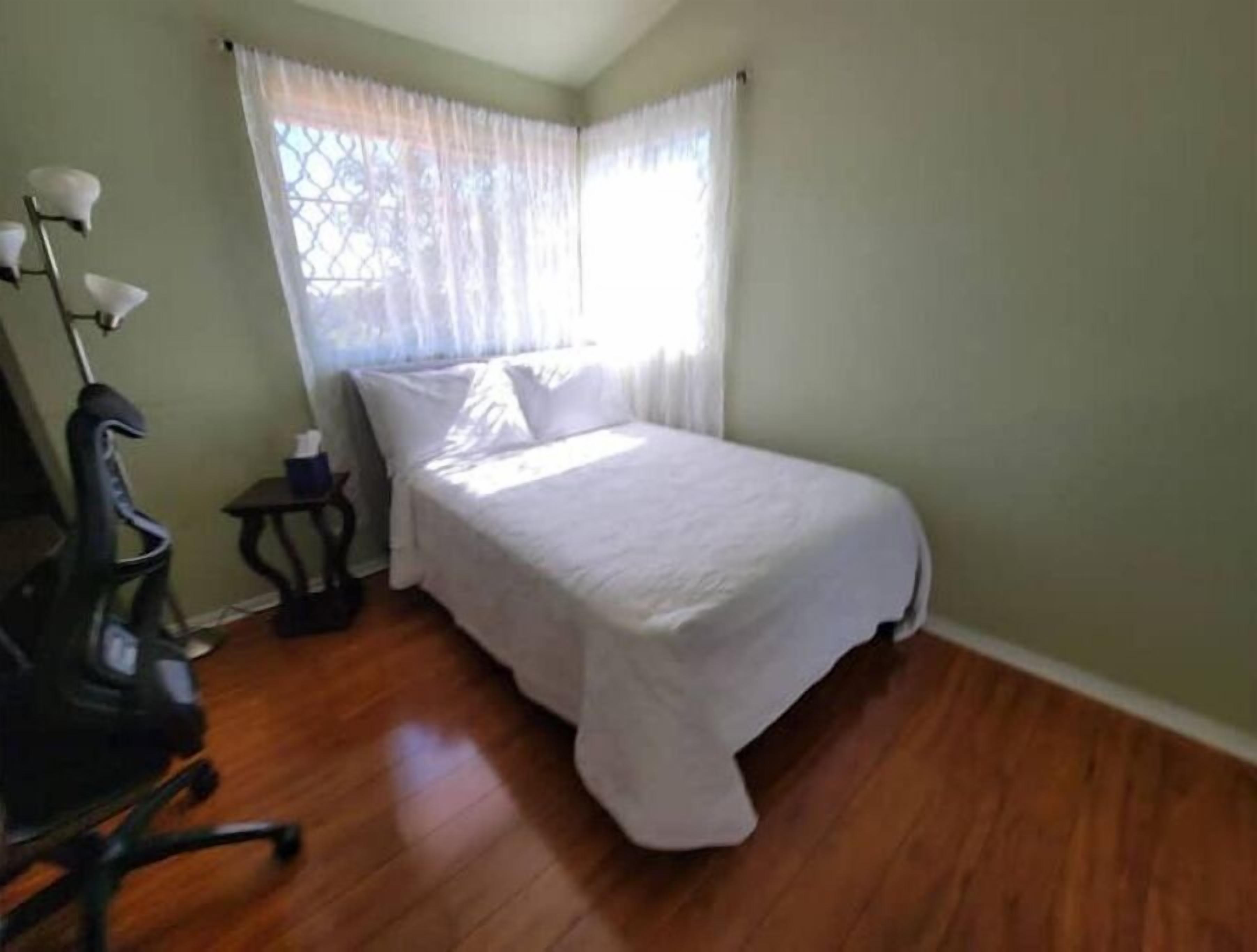 Quarto pequeno e bem organizado, com uma cama de solteiro, uma cadeira, uma mesinha e um abajur.