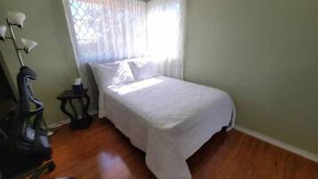 Un dormitorio pequeño y ordenado con una cama individual, una silla, una mesita y una lámpara.