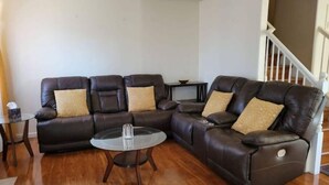 Una sala de estar con un sofá modular, una mesa de centro de vidrio y una mesita auxiliar.