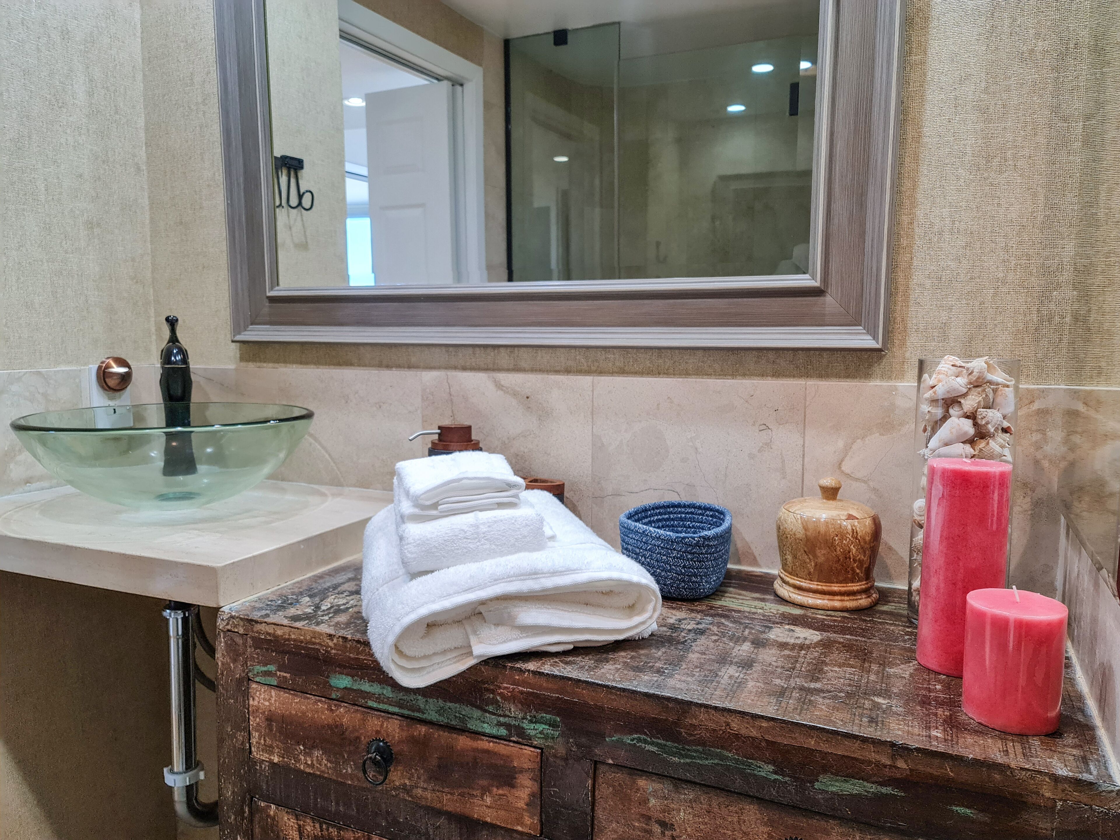 Une salle de bain avec un lavabo en verre, un meuble-lavabo en bois, un miroir et des articles de toilette posés sur le comptoir.