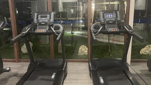 Two treadmill machines with digital displays, positioned in front of a glass wall with a view of an indoor garden and exercise equipment.