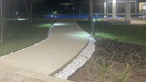 A nighttime outdoor area with a paved walkway, a covered seating area, and a building in the background.
