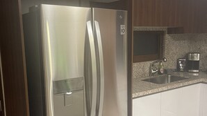 A stainless steel refrigerator in a kitchen with wooden cabinets and a granite countertop.