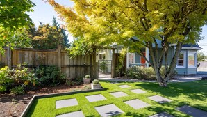 Un jardin bien entretenu, avec un chemin de pierres, une clôture en bois et un petit abri de jardin.
