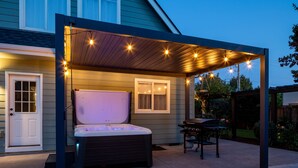 Un patio couvert avec un jacuzzi, des guirlandes lumineuses et un barbecue.