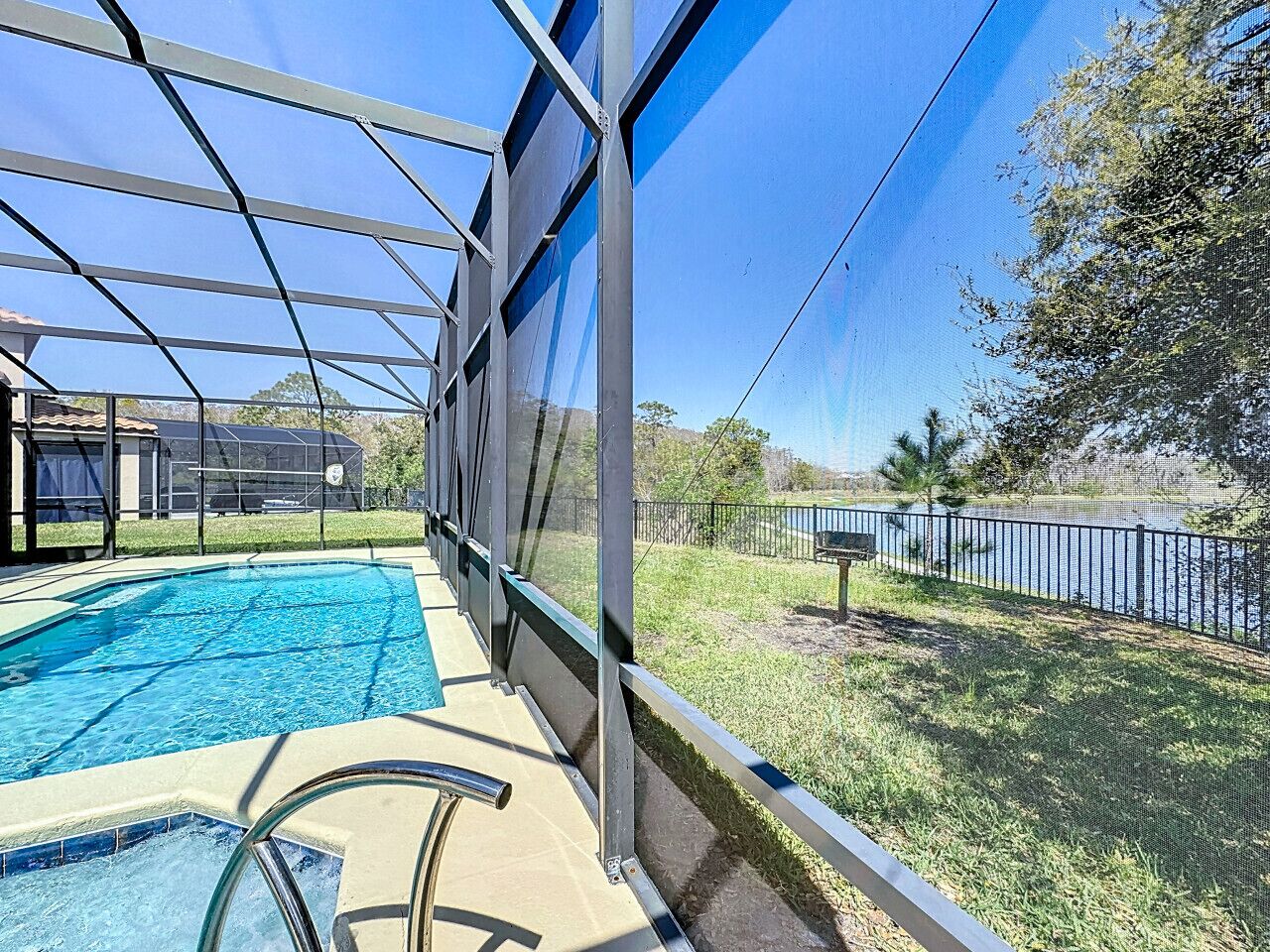 A swimming pool with a glass enclosure, surrounded by a grassy area and a body of water.
