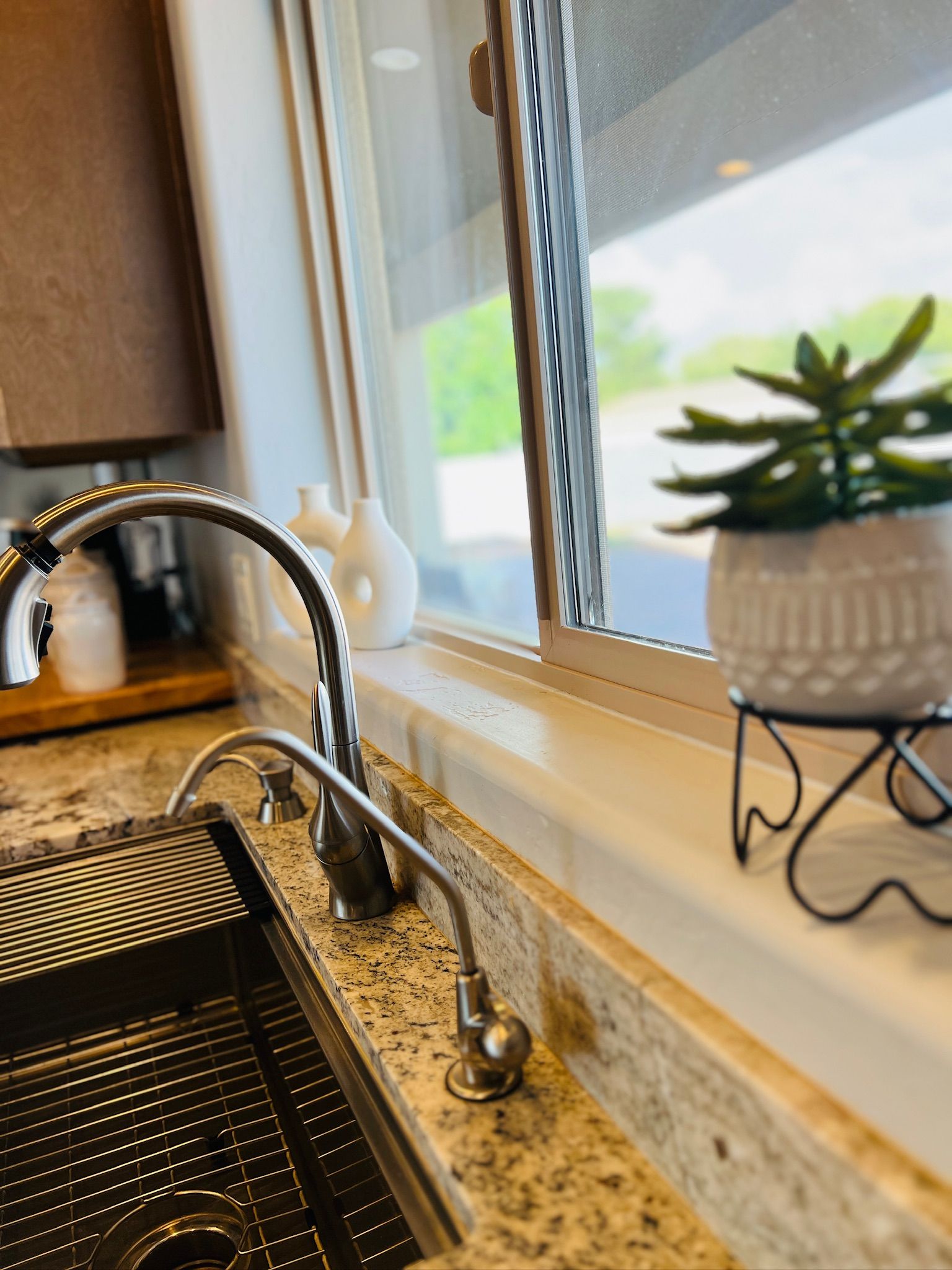 A kitchen sink with a modern faucet, a granite countertop, and a window with a view of greenery outside.