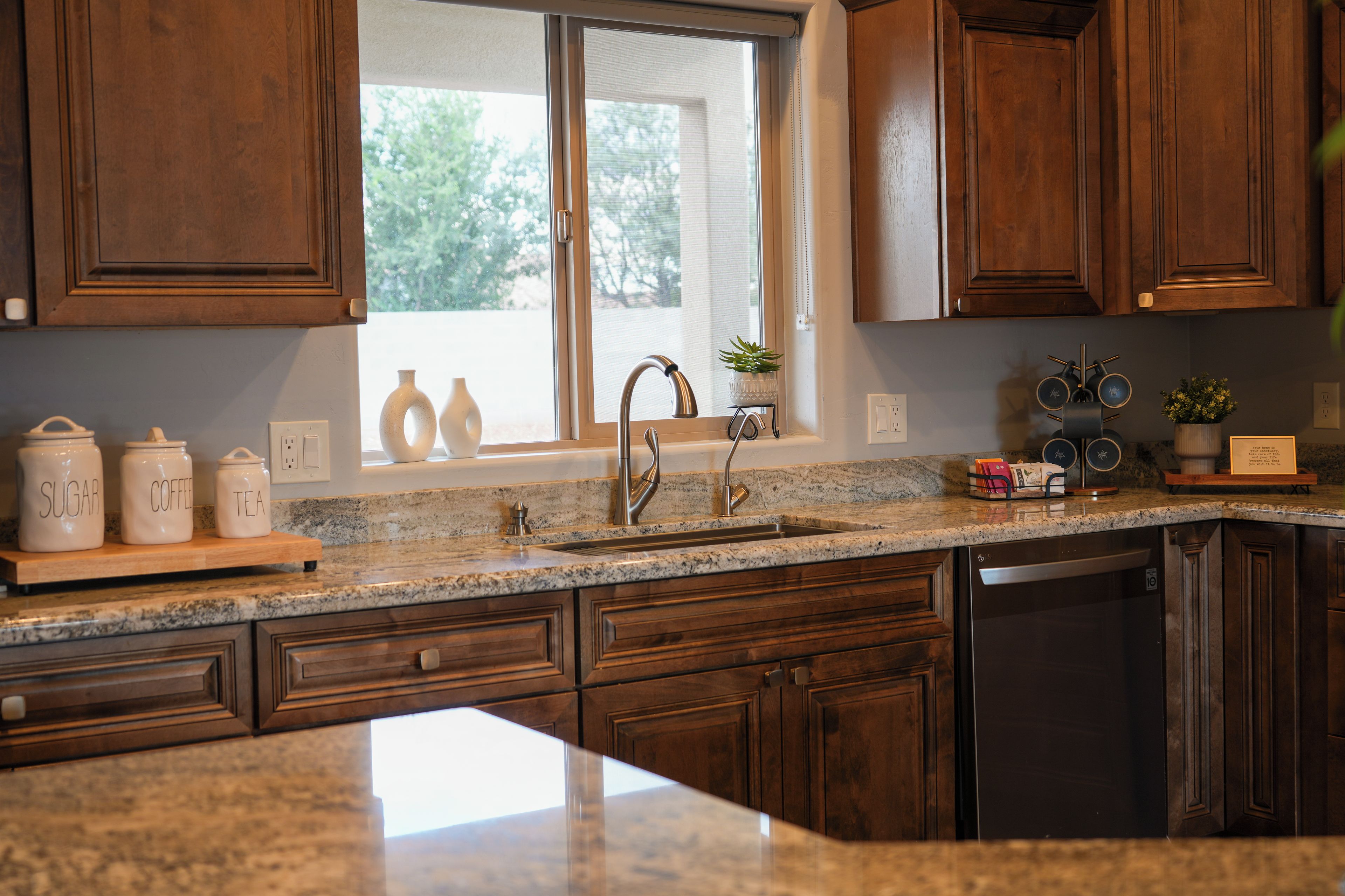 Una cocina con armarios de madera, encimera de granito, pileta de acero inoxidable y ventana con vista a árboles.