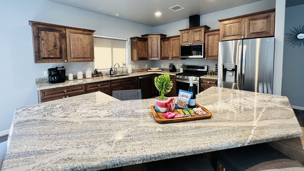 A kitchen with granite countertops, wooden cabinets, stainless steel appliances, and a welcome sign on the island.