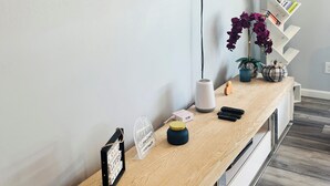 A modern living room with a mounted TV, a wooden console table, a white shelving unit, and a potted plant.
