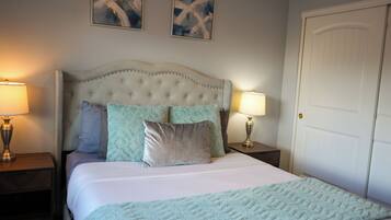 A bedroom with a tufted headboard, two bedside tables with lamps, a door, and two abstract paintings on the wall.