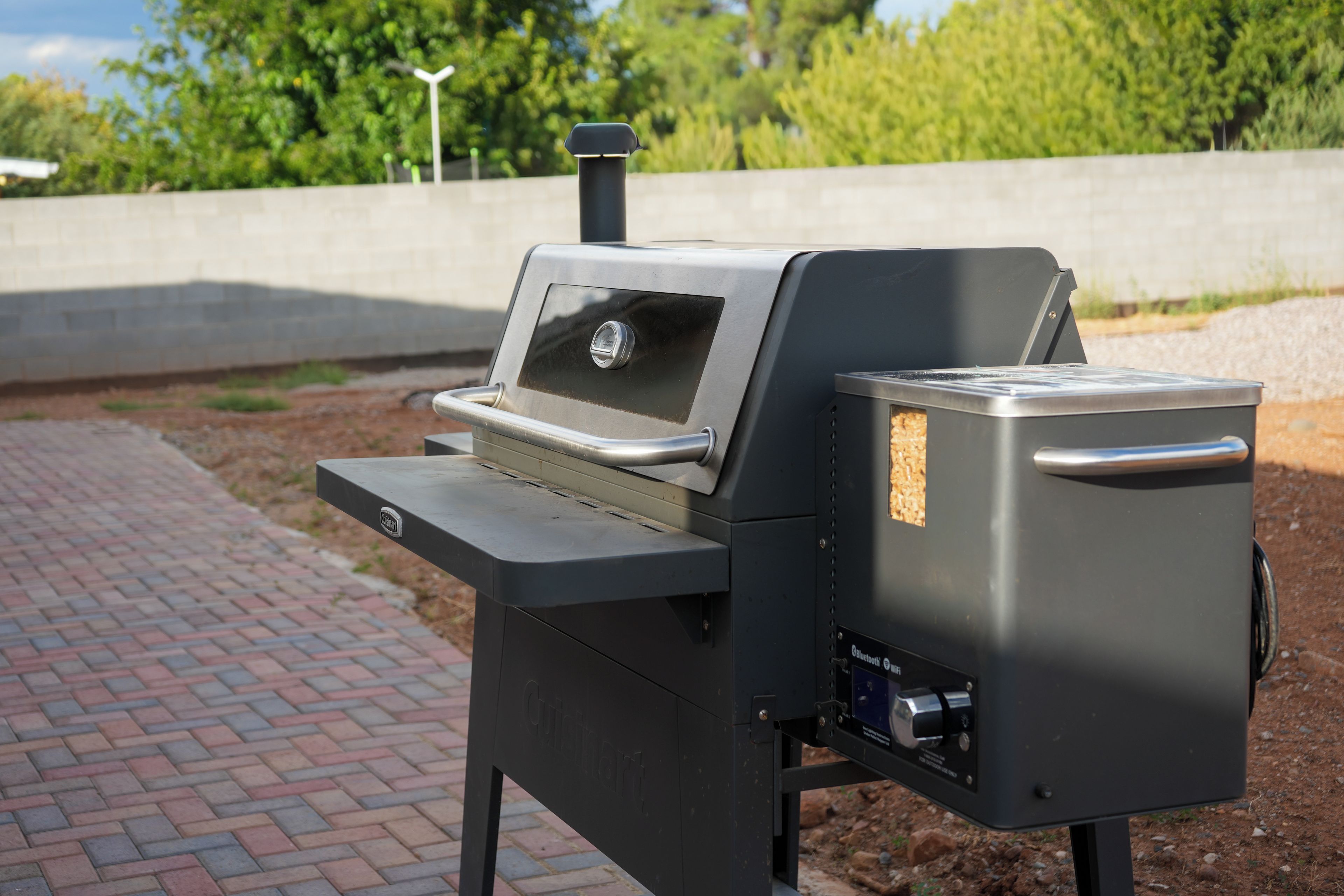 A portable grill with a digital display, a side compartment, and a handle.