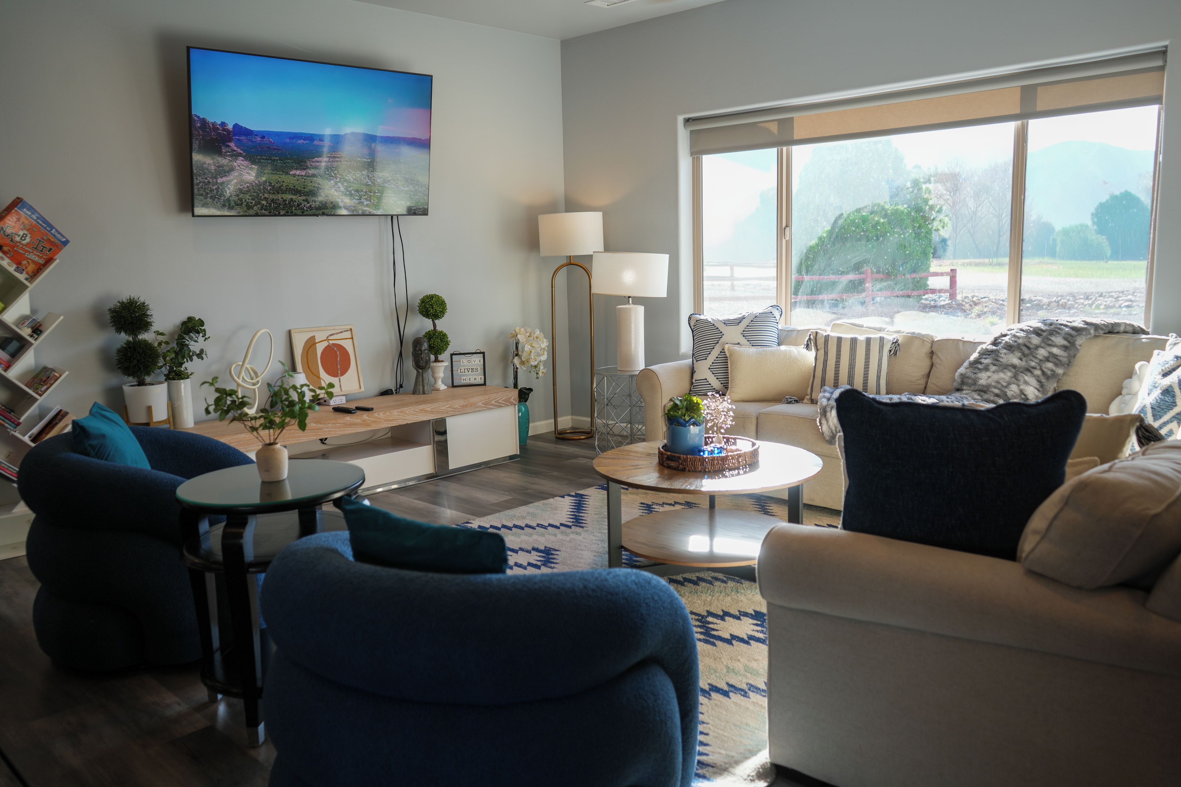 Ein modernes Wohnzimmer mit Flachbildfernseher an der Wand, einer Sofagarnitur, einem Couchtisch und einem großen Fenster mit Blick ins Freie.