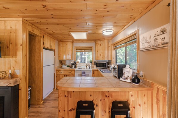 A wooden cabin kitchen with a central island, a refrigerator, microwave, stove, and a sink. - Cozy Pines Hideaway- BBQ, fire-pit, zip-line, and fireplace (Prescott)