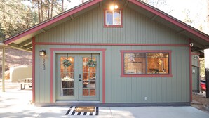 A small, single-story building with a red roof and a green facade, featuring a front door with glass panels and a welcome mat.