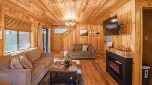 A cozy wooden cabin interior with a sofa, a coffee table, a fireplace, and a television mounted on the wall.