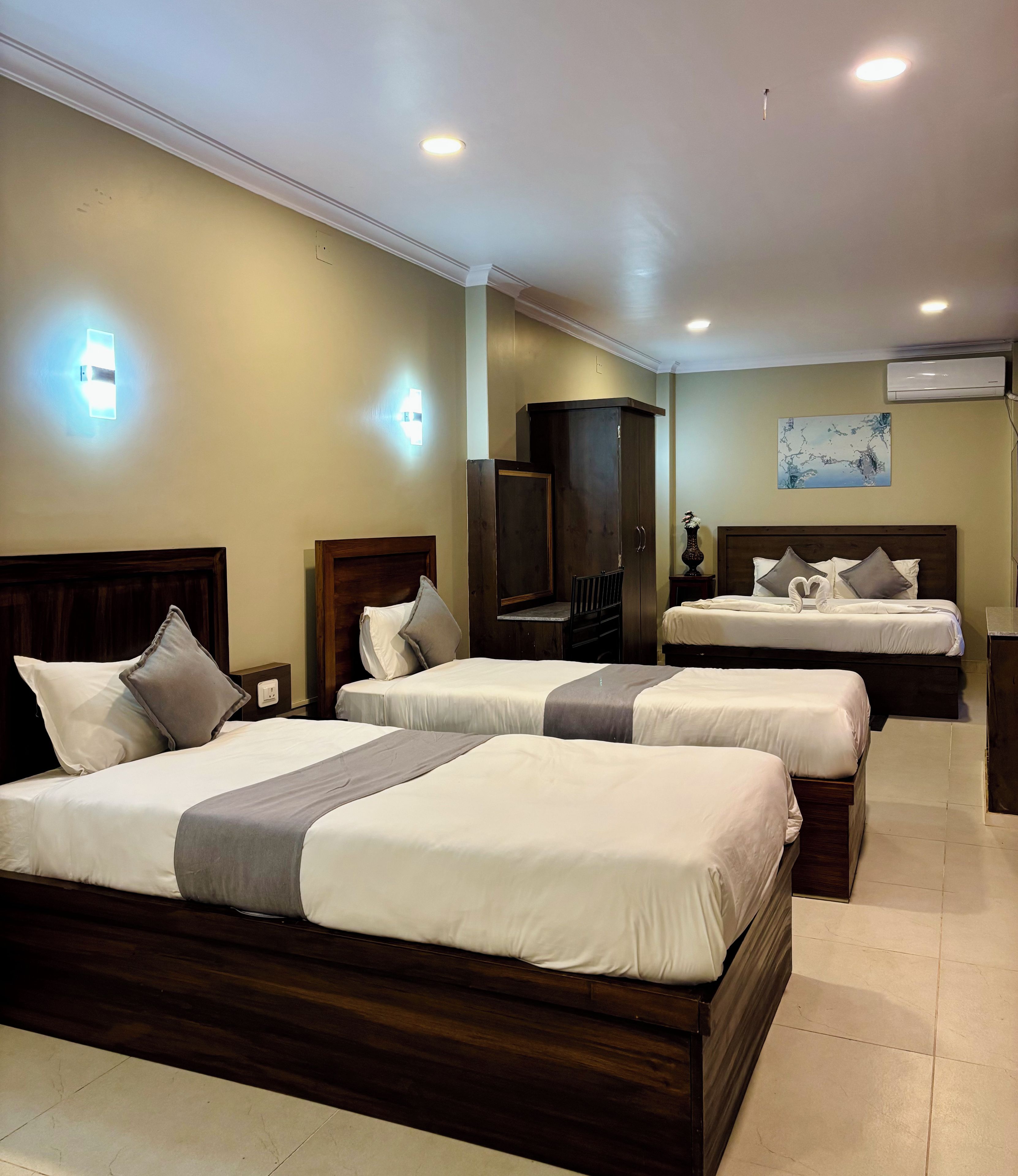 A hotel room with three beds, a flat-screen TV, a painting on the wall, and an air conditioning unit.