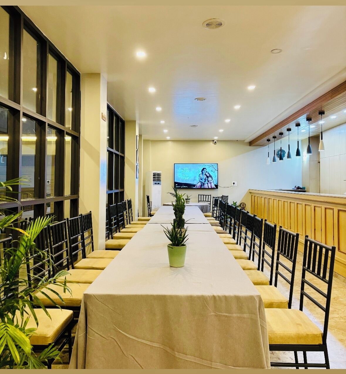 A conference room with a long table, chairs, a TV screen, and a plant.