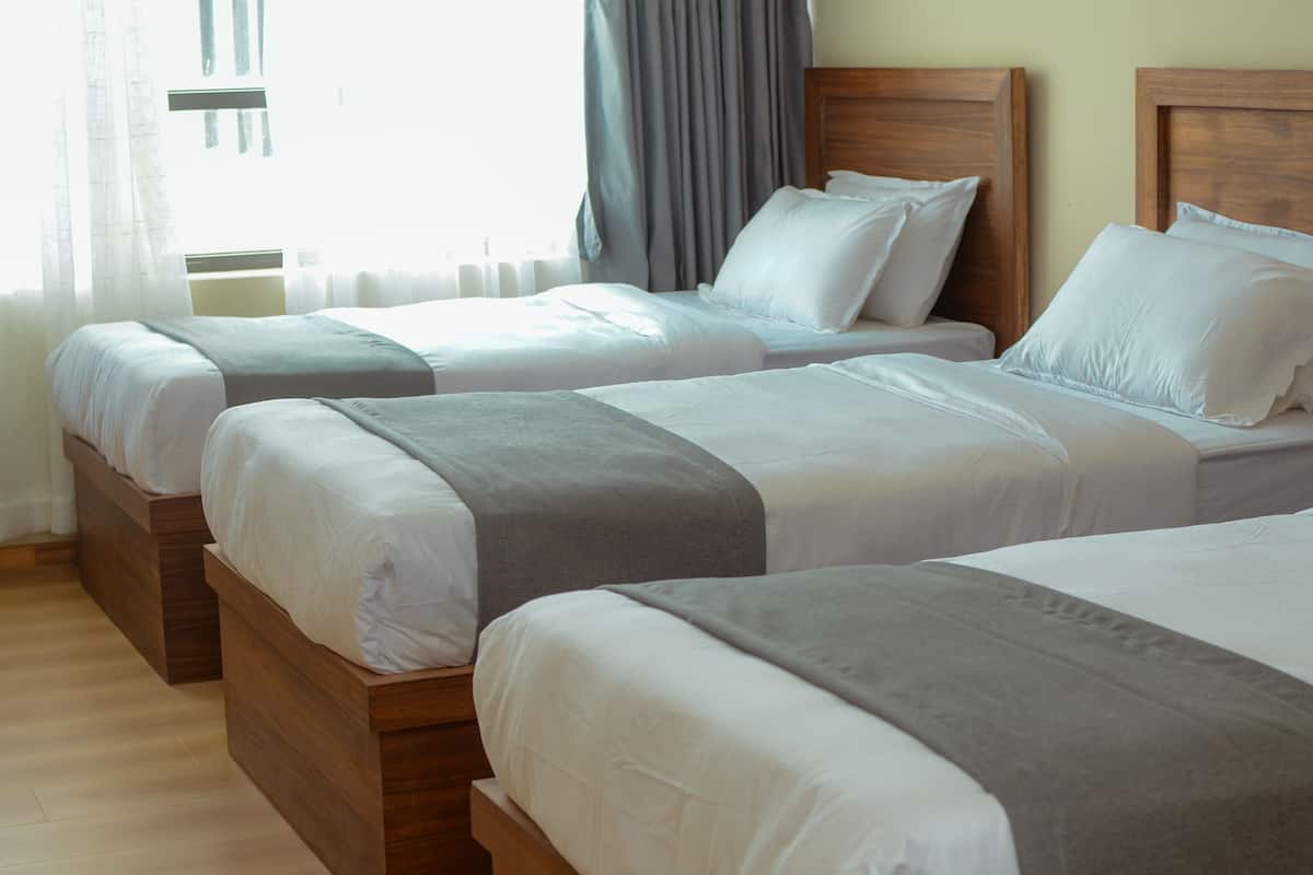 Quarto de hotel com três camas de madeira, cada uma com roupa de cama branca e mantas cinzentas.
