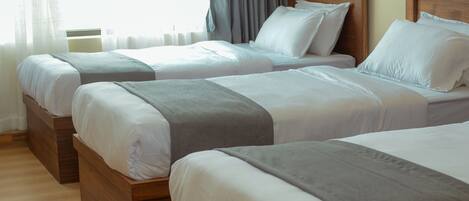 Ett hotellrum med tre sängar i trä, alla med vita sängkläder och gråa plädar.