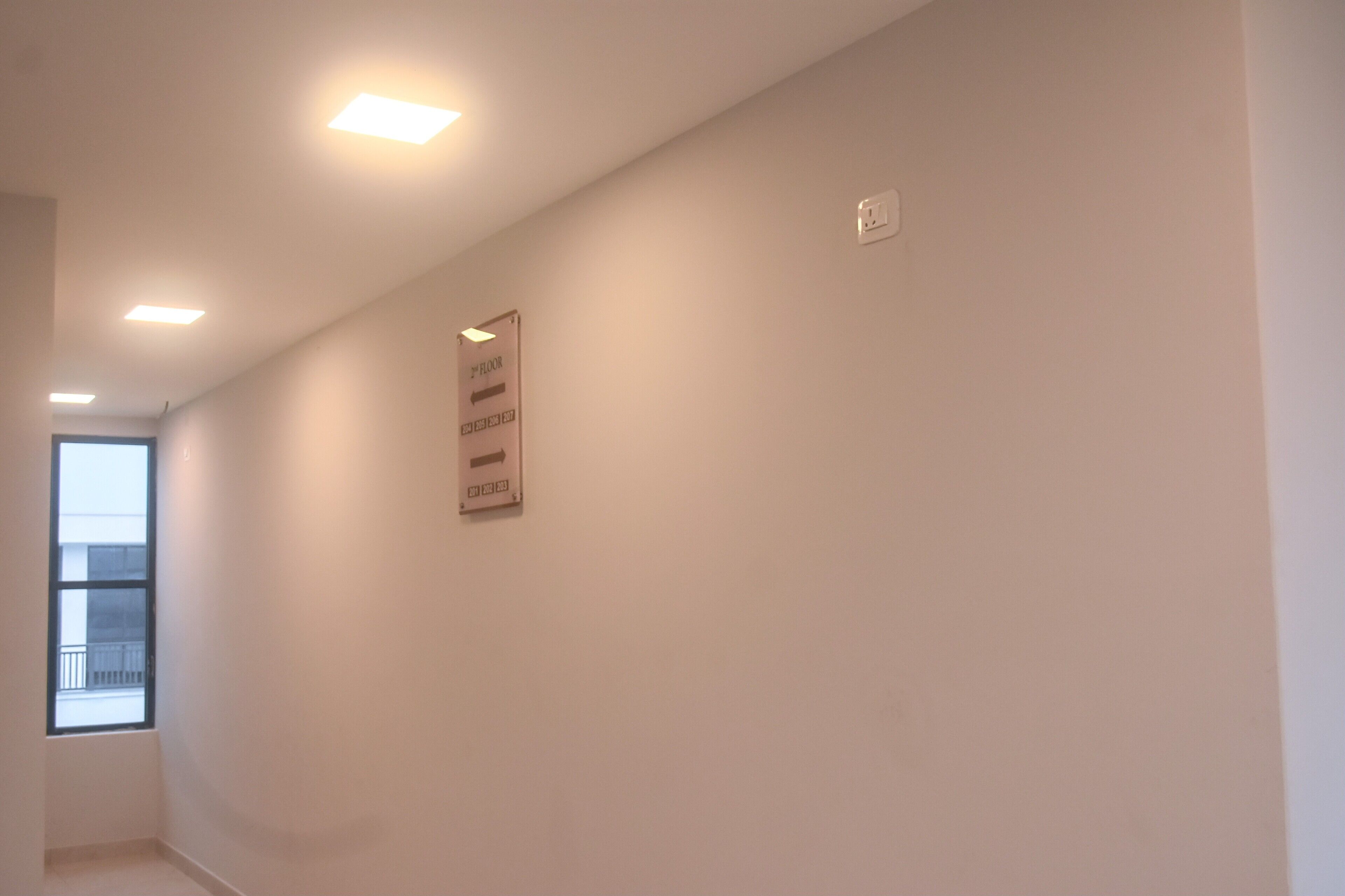 A narrow hallway with white walls, a sign on the wall, and a window on the left.
