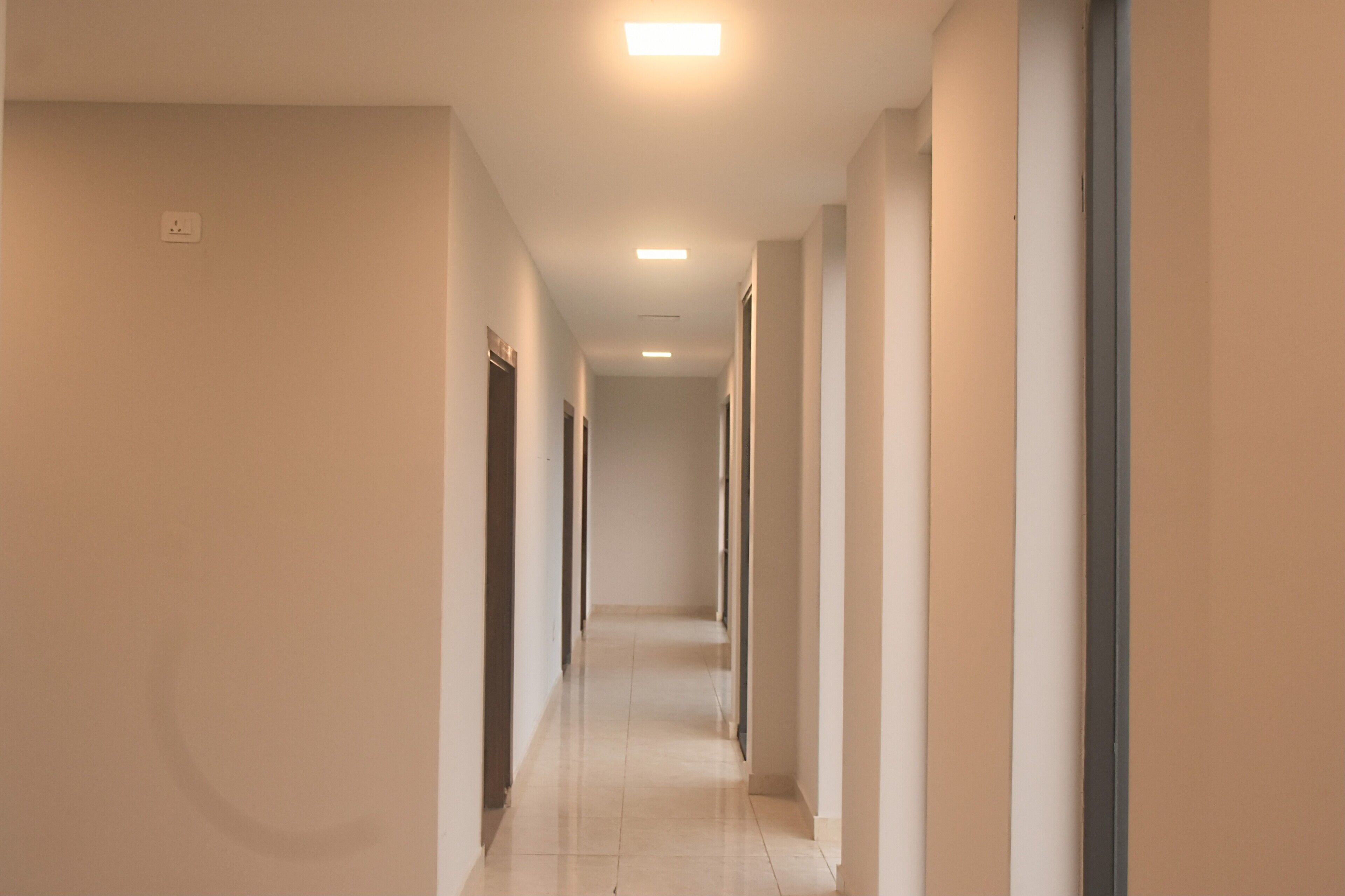A long, narrow hallway with a series of doors on one side and a light source at the end.