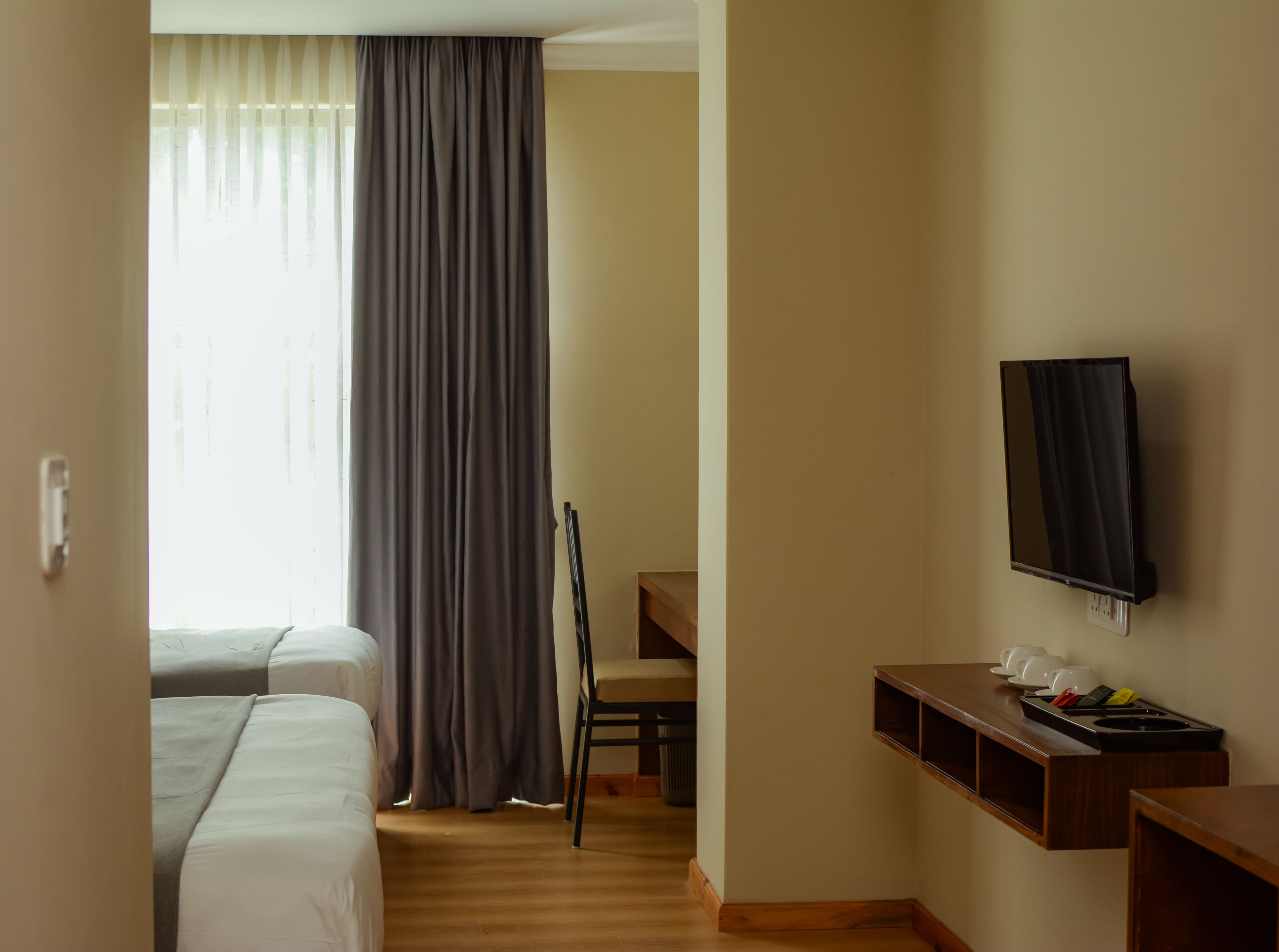 Habitación de hotel con dos camas, un escritorio, un televisor de pantalla plana, una silla y un estante pequeño con tazas y un teléfono.
