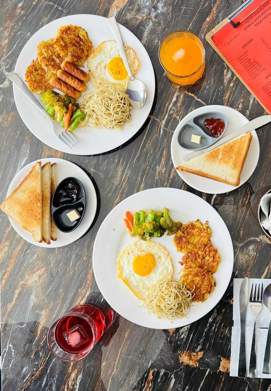 A table with plates of food including eggs, noodles, and vegetables, along with toast and a menu.
