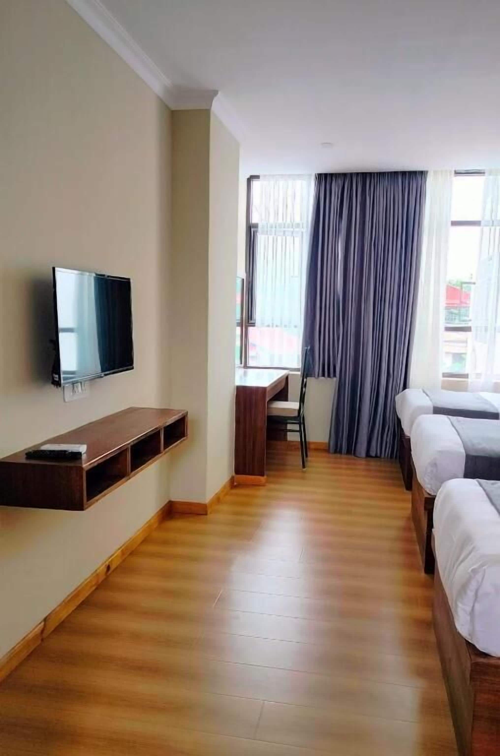 A hotel room with a TV mounted on the wall, wooden flooring, a desk, and two beds.
