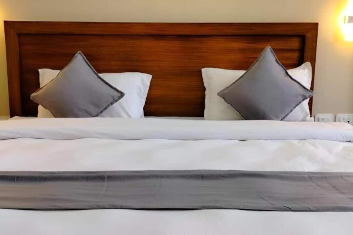 Cama bem arrumada com cabeceira de madeira, duas almofadas e um edredom.