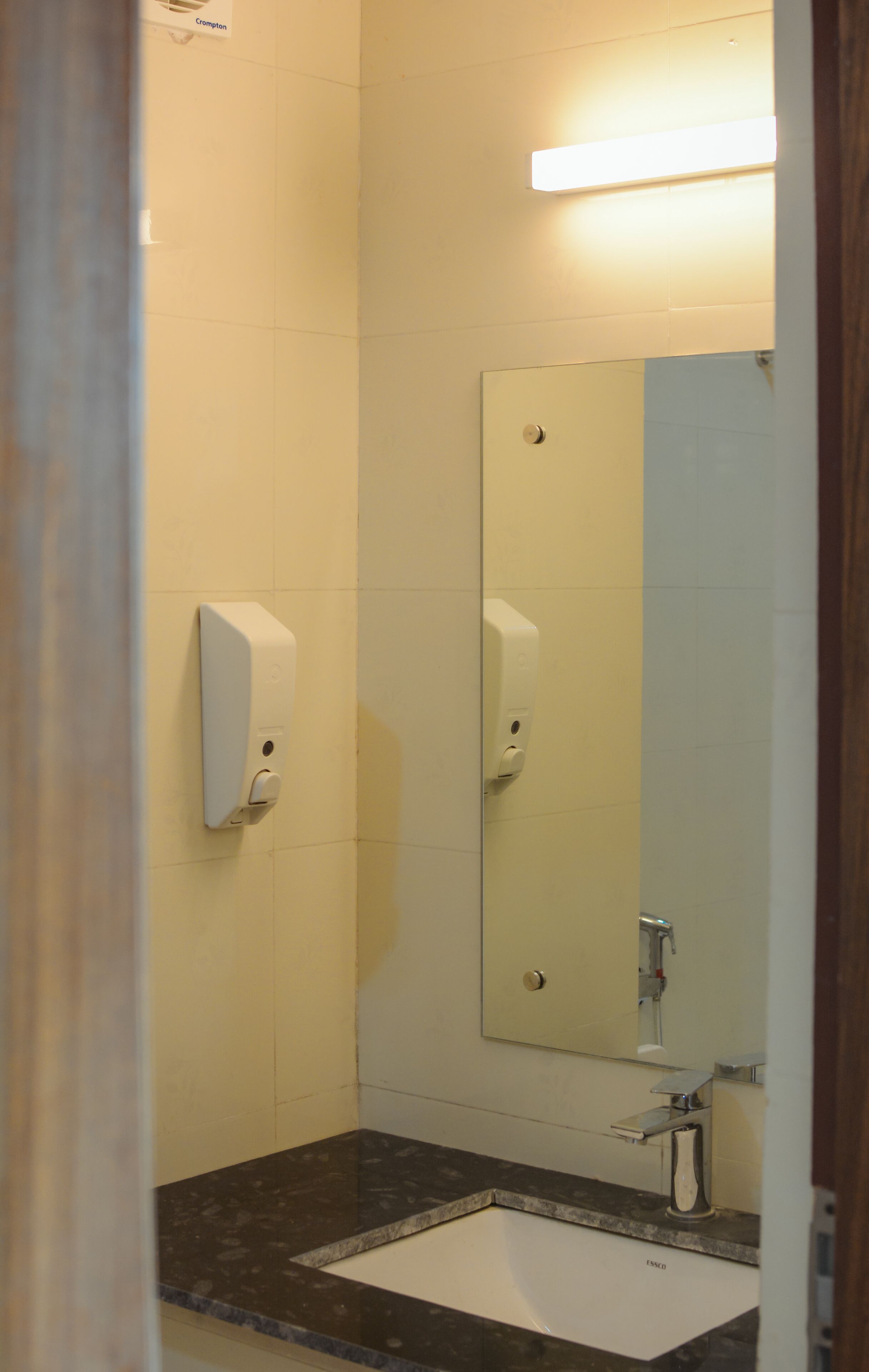 Un baño con un lavamanos blanco, un espejo, un dispensador de jabón y un inodoro.