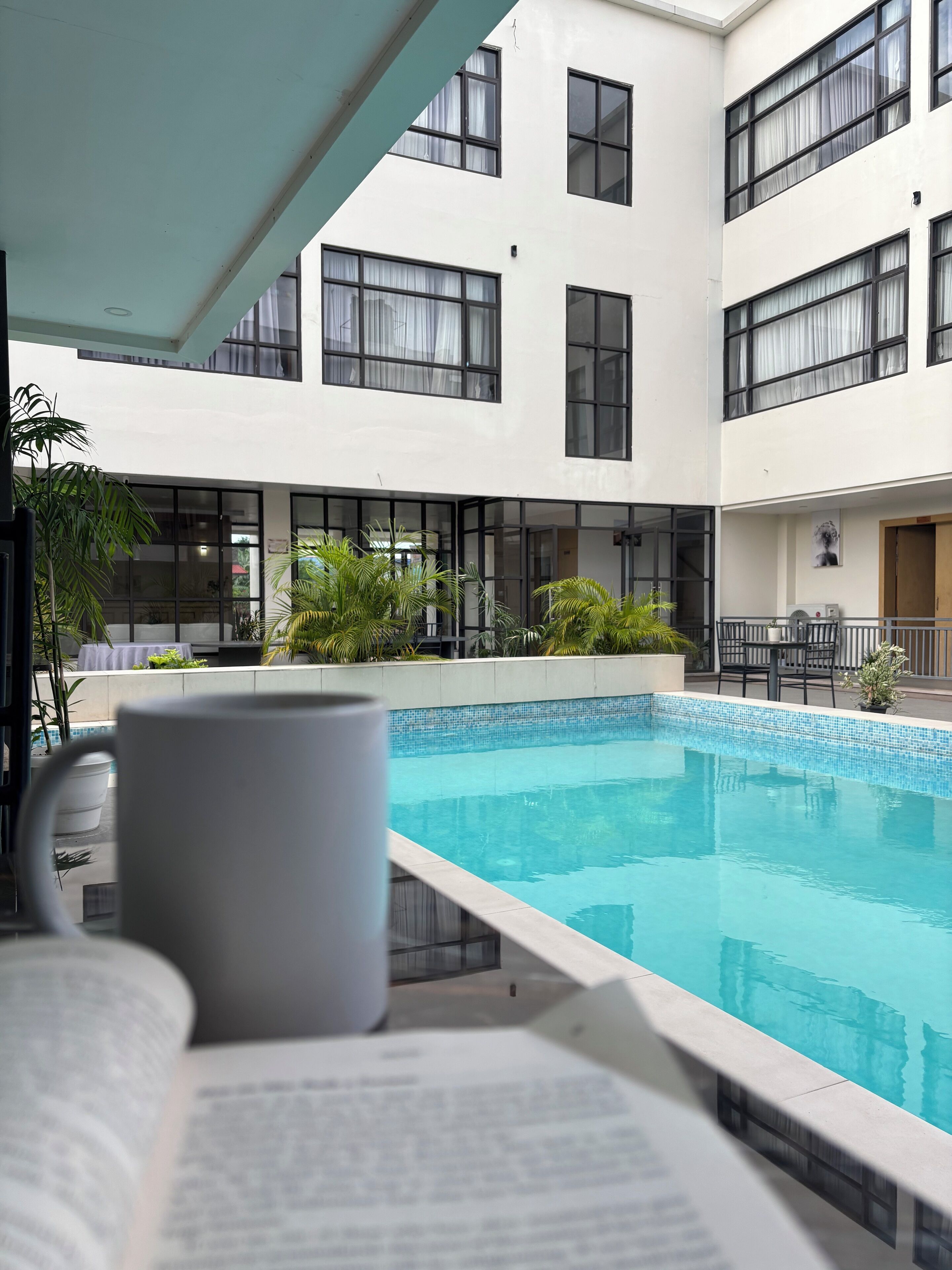A modern hotel with a pool area, featuring a clear blue pool, potted plants, and a seating area with a table and chairs.