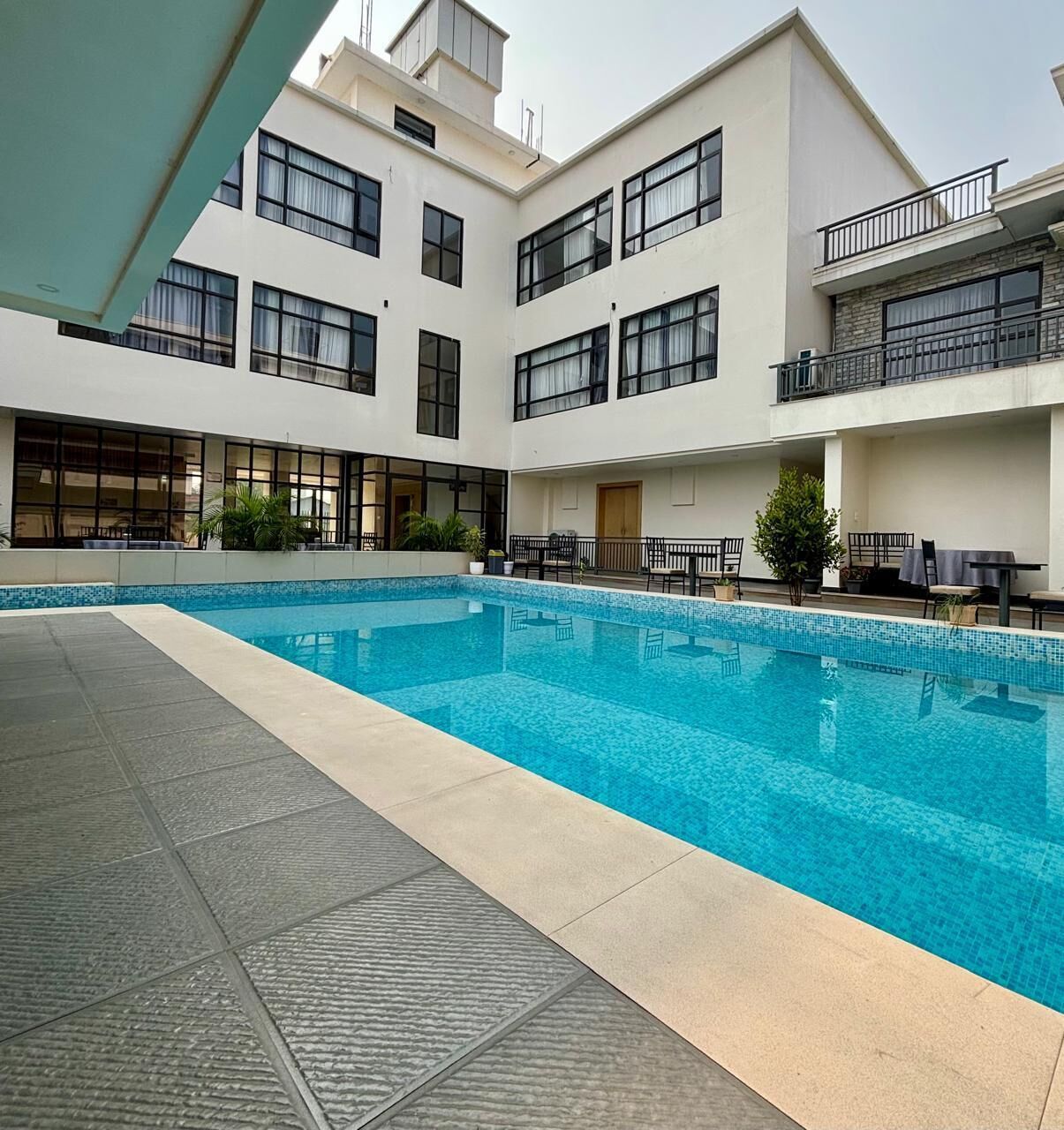 A modern building with a central swimming pool, multiple balconies, and outdoor seating areas.