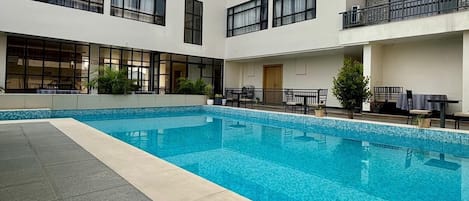A modern building with a central swimming pool, multiple balconies, and outdoor seating areas.