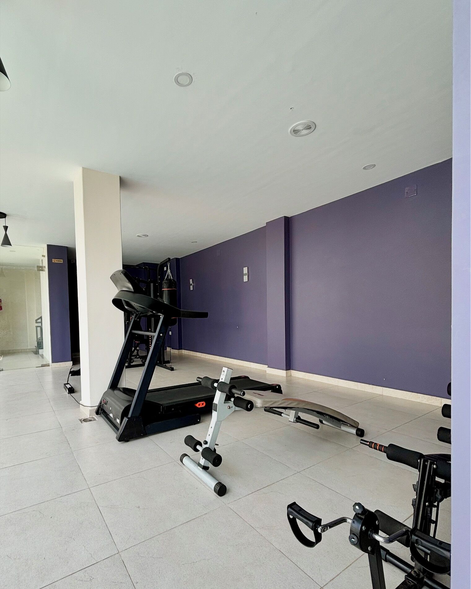 Un gimnasio con cinta de correr, banco de pesas y diversos equipos de ejercicio.