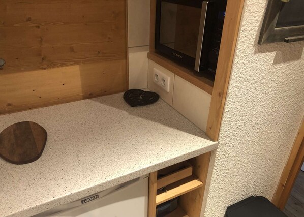 A kitchenette with a microwave, a wooden countertop, and a small drawer unit.
