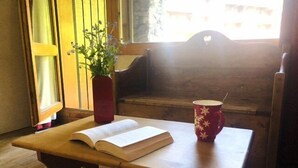 Un banco de madera con un libro y una taza, al lado de una ventana con persianas.