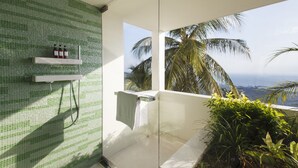 A modern bathroom with a green mosaic wall, a shower, and a view of palm trees and the ocean.
