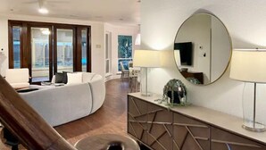 Een moderne hotelkamer met een gebogen bank, een houten bankje, een ronde spiegel en een console tafel met een decoratieve krans.