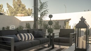 A modern outdoor seating area with a sofa, armchair, and table, surrounded by potted plants and a lantern. - Upscale Home - Heated Modern Pool, Outdoor BBQ, Large Kitchen, Up to 8 Guests! (Las Vegas)
