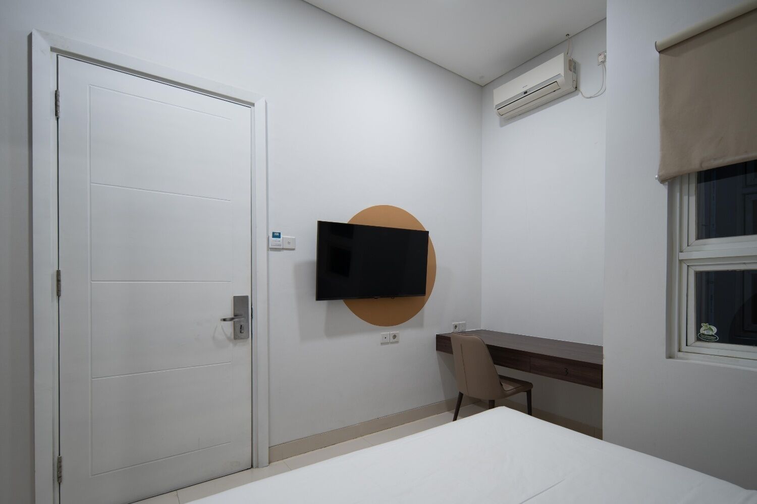 Habitación de hotel con cama, escritorio, silla, televisor montado en la pared y unidad de aire acondicionado.