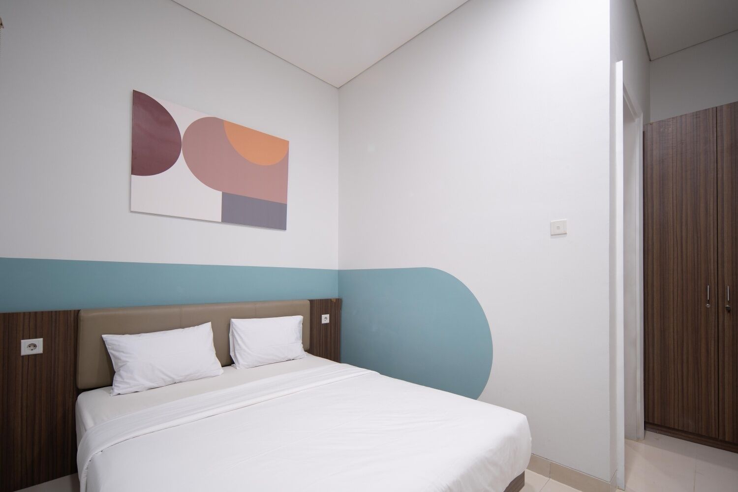Un dormitorio con una cama, una obra de arte abstracta colgada en la pared y un armario de madera.