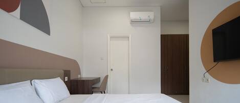 A hotel room with a bed, a desk, a chair, an air conditioning unit, and a television mounted on the wall.