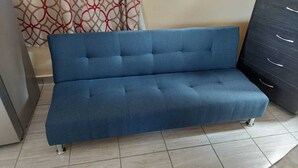 A blue sofa with a tufted design, positioned on a tiled floor.